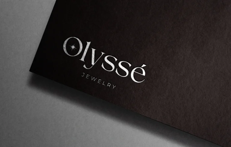 Olyssé Jewelry için tasarlanan logo, markanın lüks ve zarif çizgisini yansıtan modern bir imza niteliğinde. Siyah zemin üzerindeki parlak gümüş detaylar, premium marka kimliğini güçlendirirken, özgün tipografi Olyssé’nin zamansız ve ulaşılabilir lüks anlayışını ön plana çıkarıyor.